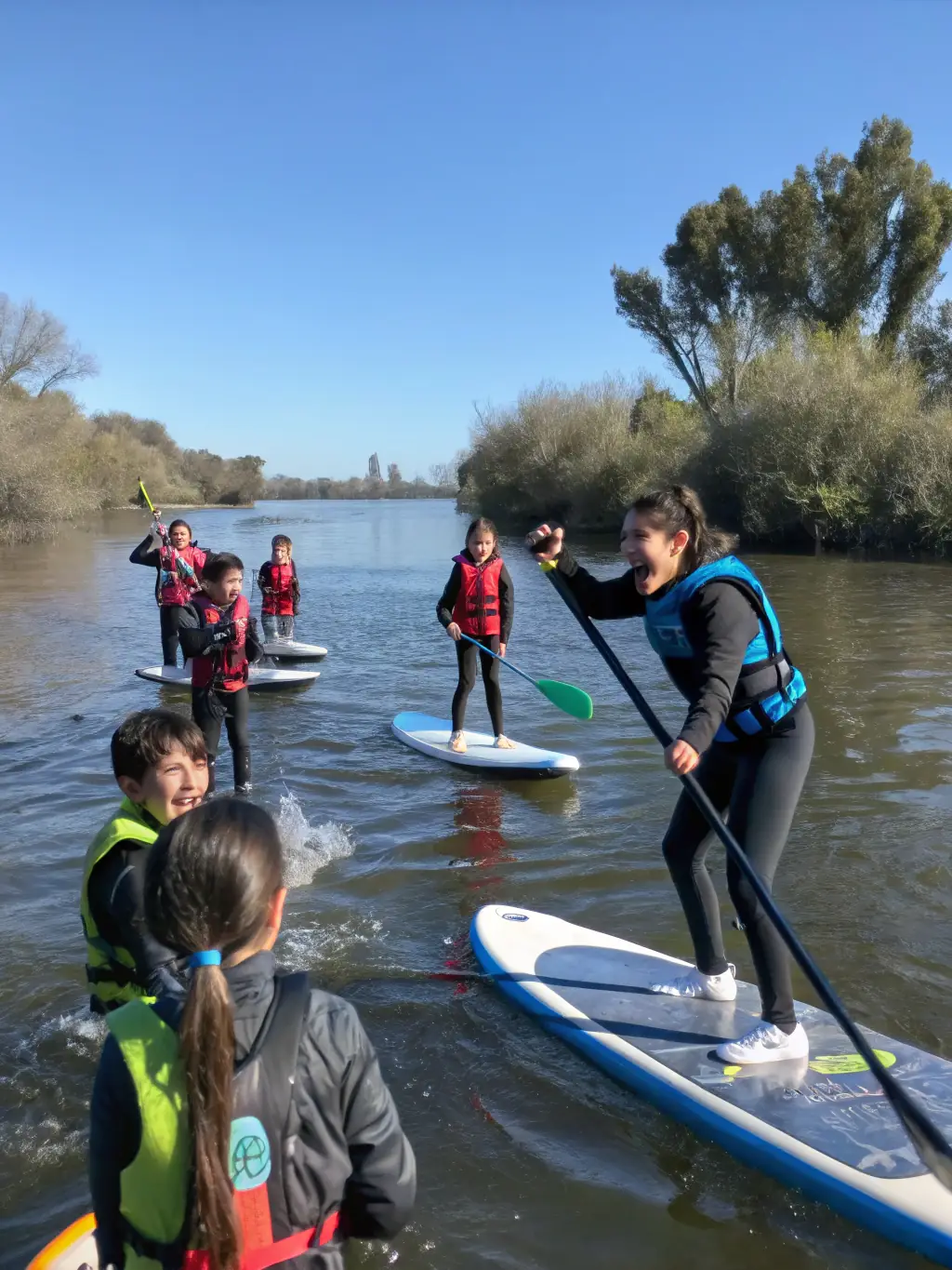 A group of children learning basic kayaking skills in a calm river, supervised by instructors, showcasing the youth program.